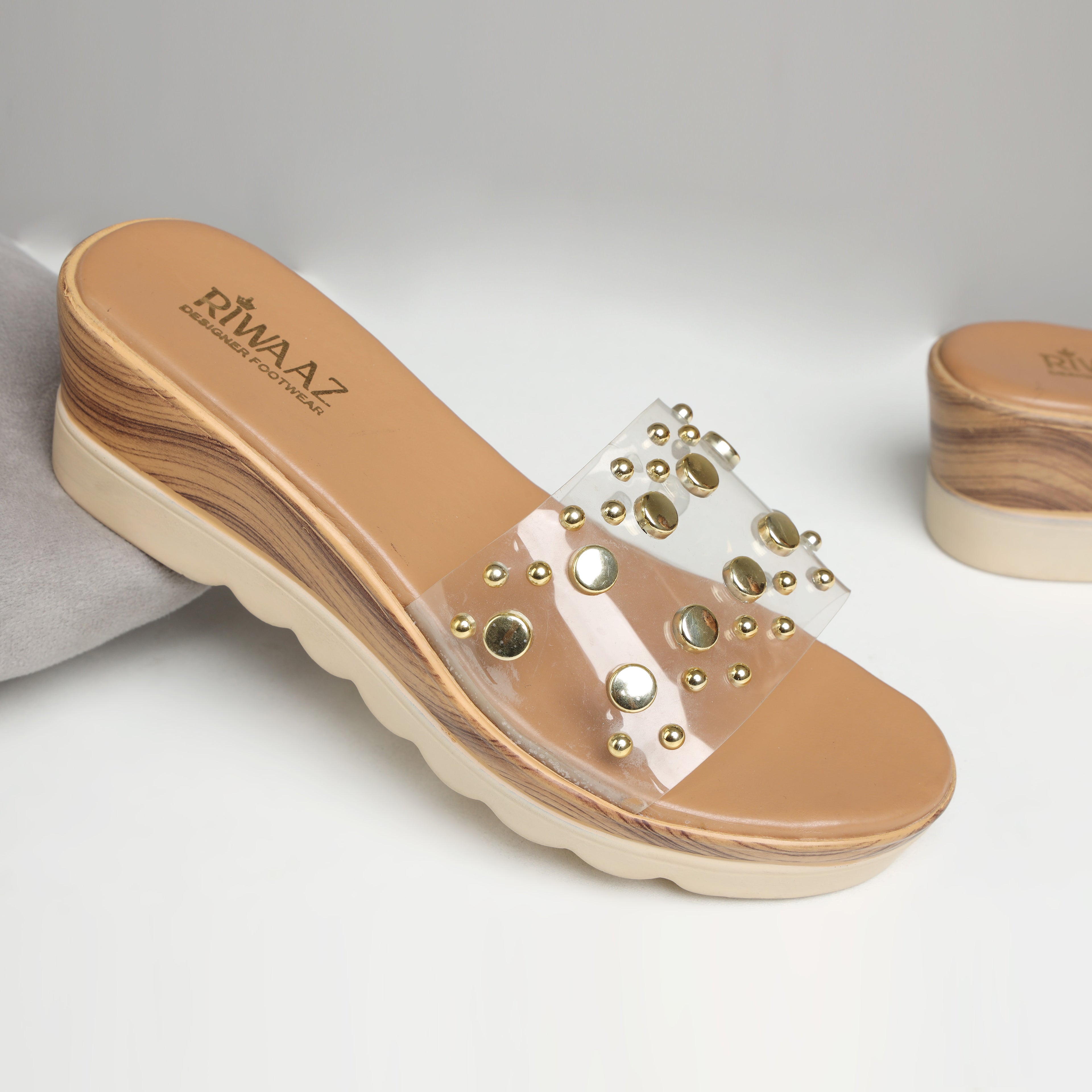 Model wearing Riwaaz Nora gold studded clear strap wedge slides with white linen wide-leg trousers – close-up foot shot