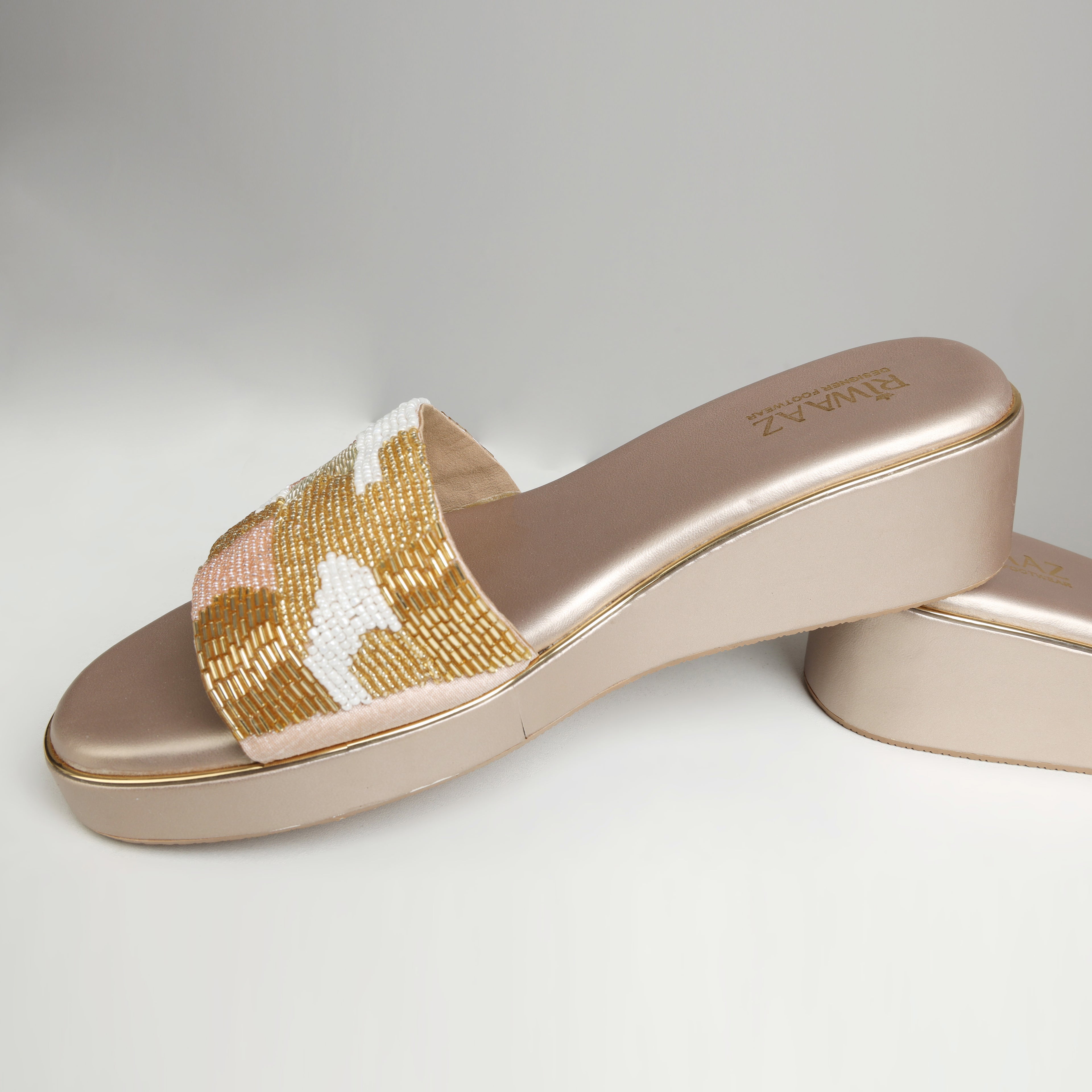Dull gold Riwaaz Gulnaar bead embroidered wedge slide with ivory, gold and blush bead work on strap – product shot on wooden display with pearls and plant in background