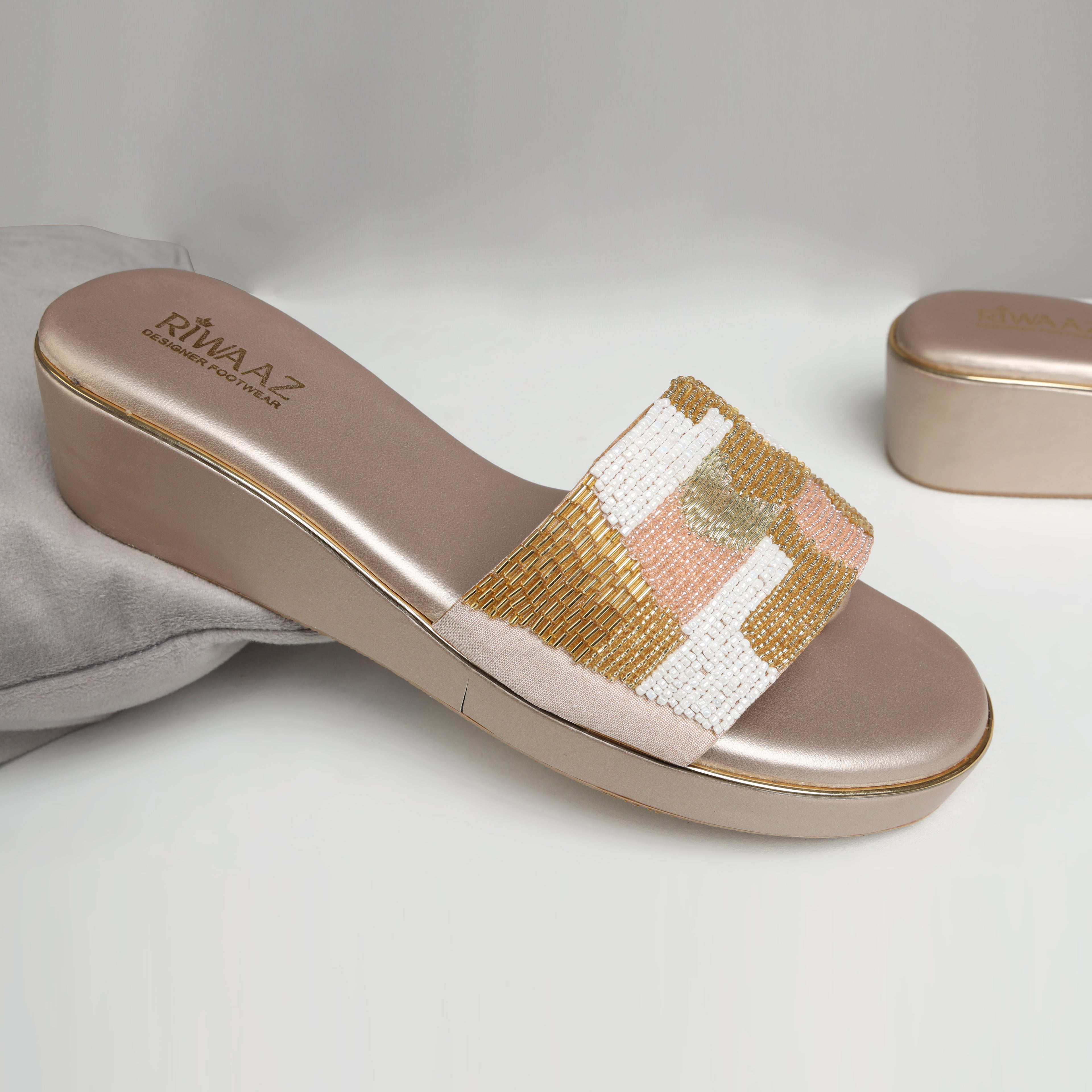 Model wearing Riwaaz Gulnaar dull gold bead embroidered wedge slides with white floral embroidered salwar – close-up foot shot on jute rug