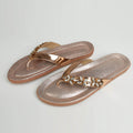 Dull rose gold Riwaaz Ziva Kundan embellished flip flop with metallic gold strap and sparkling crystal cluster embellishment – product shot on white background with grey fabric