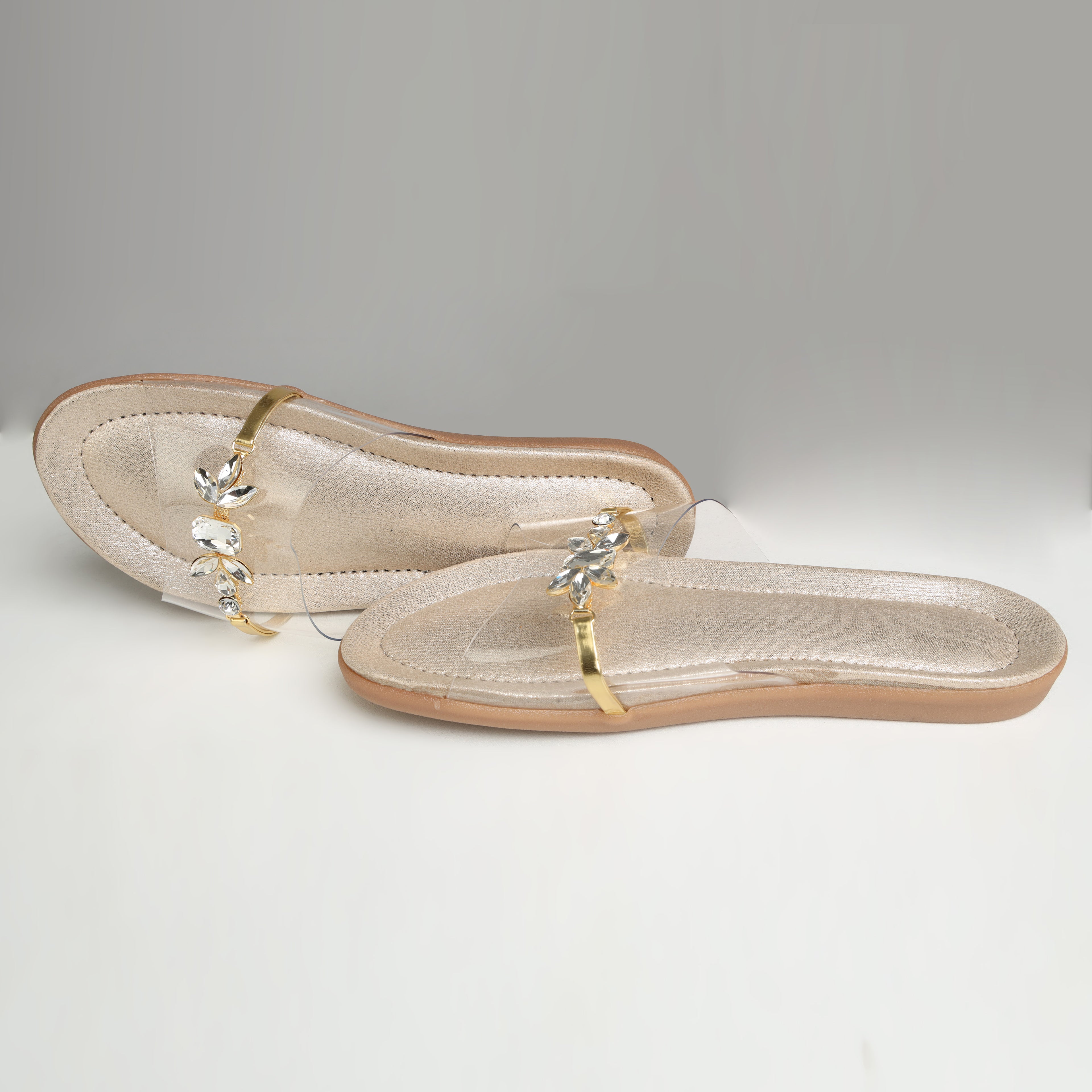 Pair of Riwaaz Ira dull gold crystal transparent strap flats – flat lay top view on grey background showing shimmer insole and crystal strap