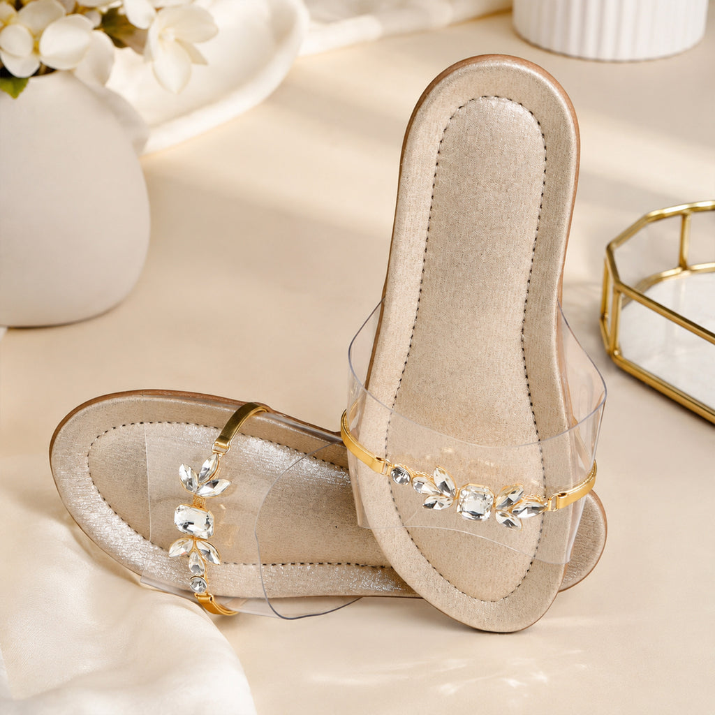 Model seated in cream kurta set wearing Riwaaz Ira dull gold crystal transparent strap flats – full lifestyle shot in lush green garden setting with rattan chair