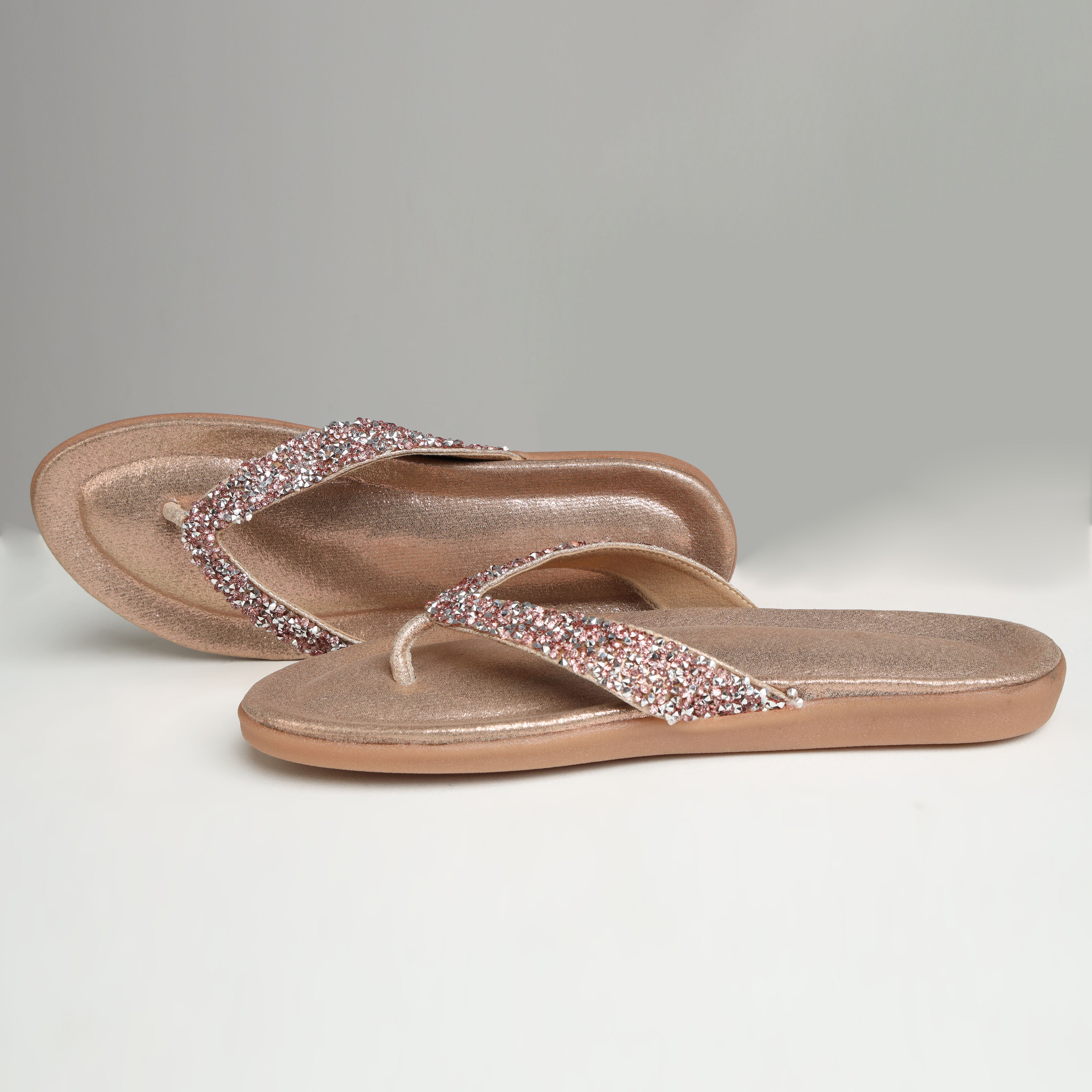 Pair of Riwaaz Aurelia dull rose gold crystal flip flops on white background – side angle showing cushioned sole profile and crystal strap detail