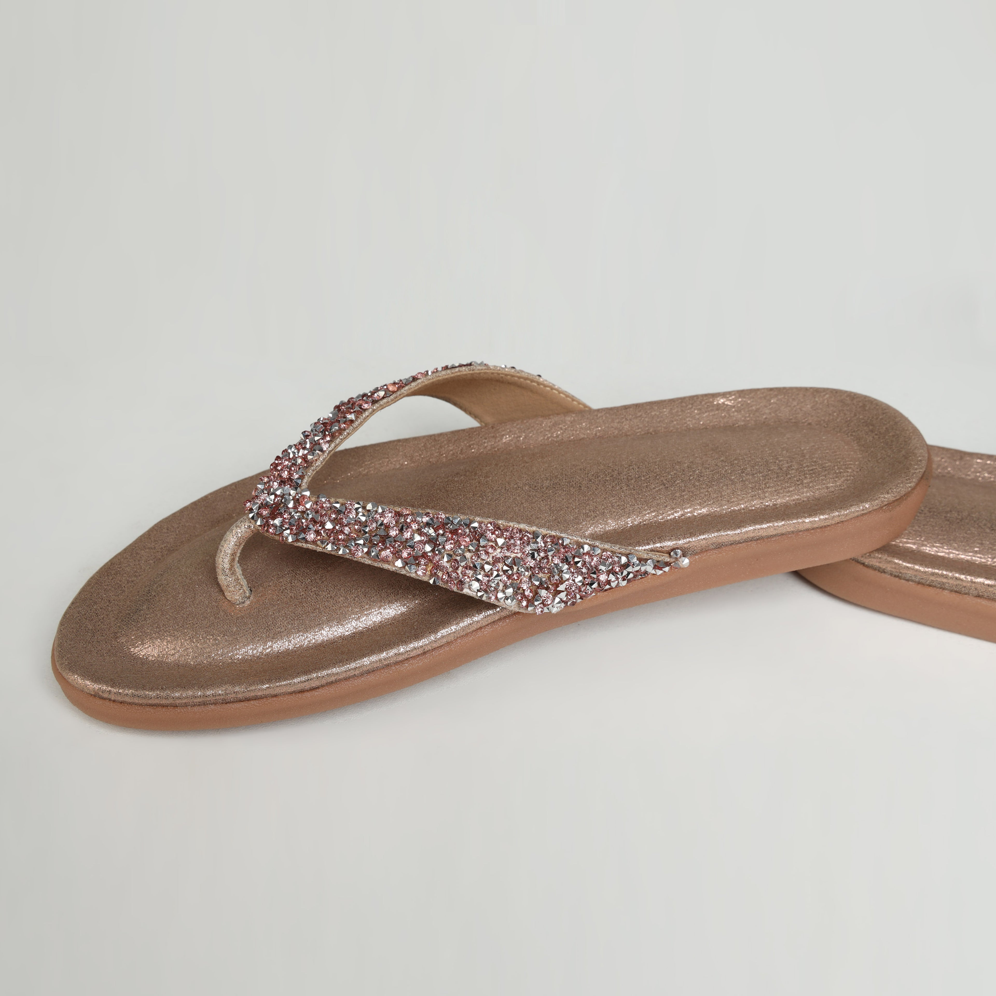 Pair of Riwaaz Aurelia dull rose gold crystal flip flops – overhead flat lay on white background showing shimmer insole and full crystal strap coverage