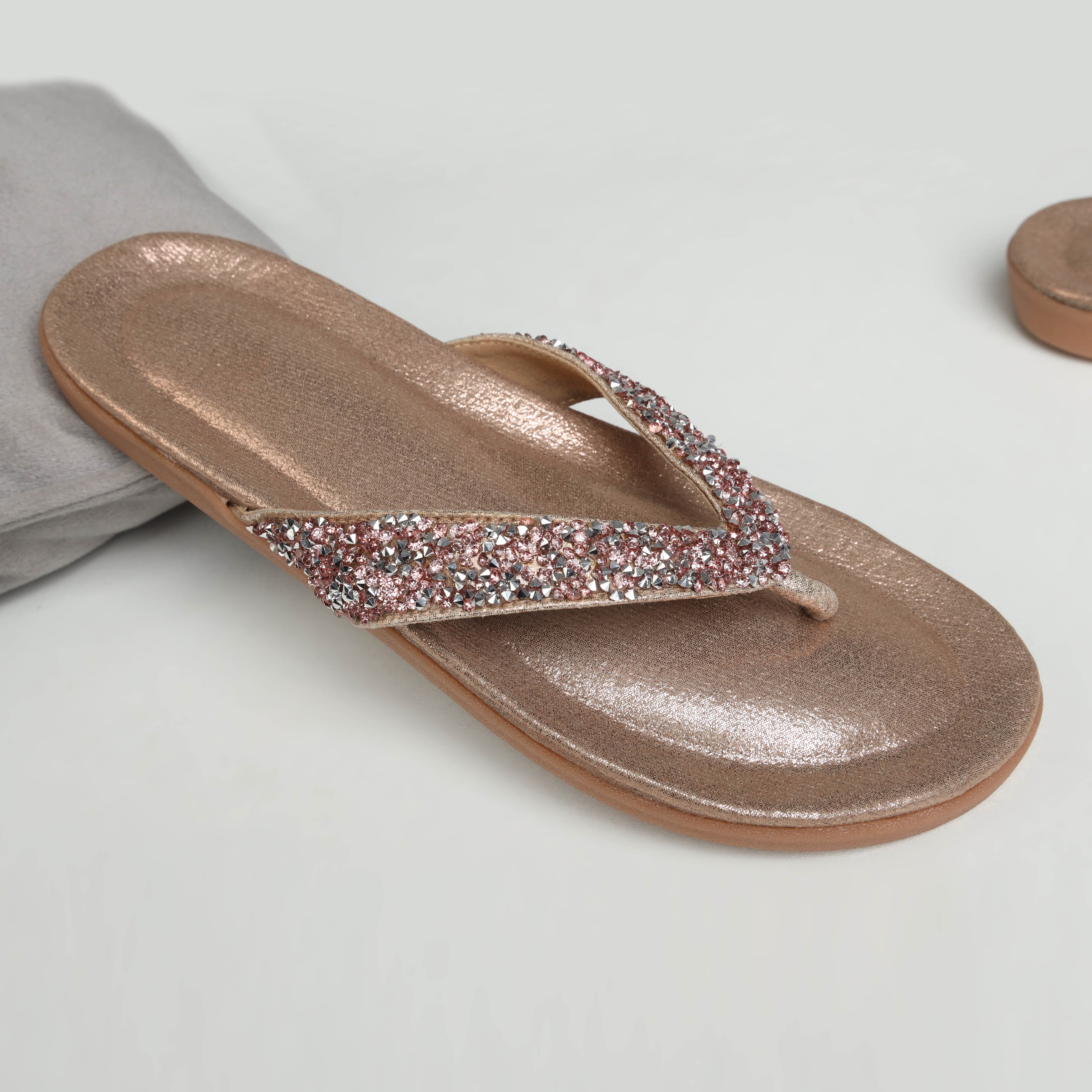 Model wearing Riwaaz Aurelia dull rose gold crystal-embellished flip flops with cream embroidered salwar – close-up foot shot on jute rug in warm Indian interior setting