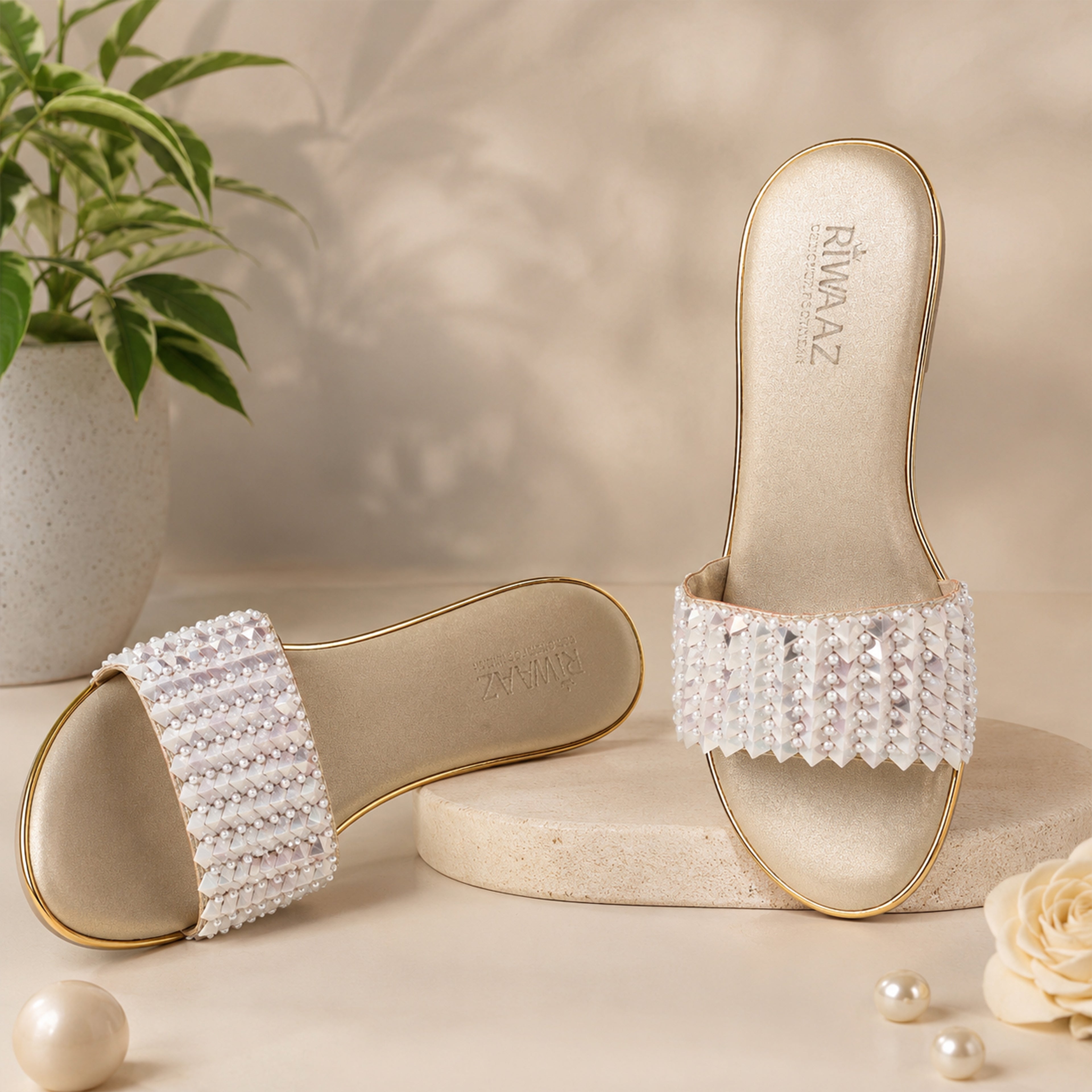 Model seated in cream embroidered kurta set wearing Riwaaz Chandni Glow dull gold pearl and sequin wedge sandals – full lifestyle shot in warm Indian interior with rattan chair and pink flowers