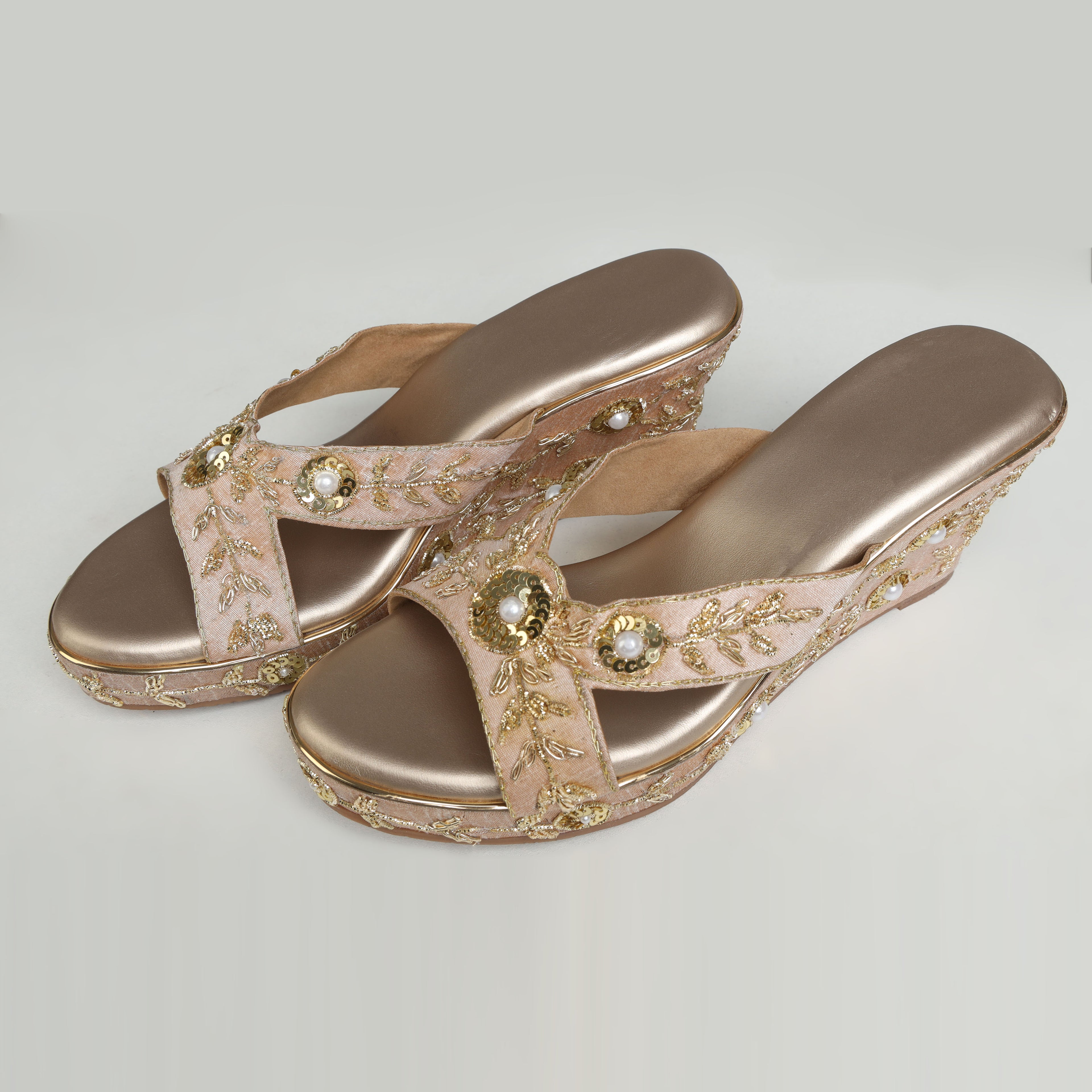 Pair of Riwaaz Noor rose gold bridal wedge heels – top-down product shot on white background showing shimmer insole and full zari embroidered cross-strap with pearl and sequin detail