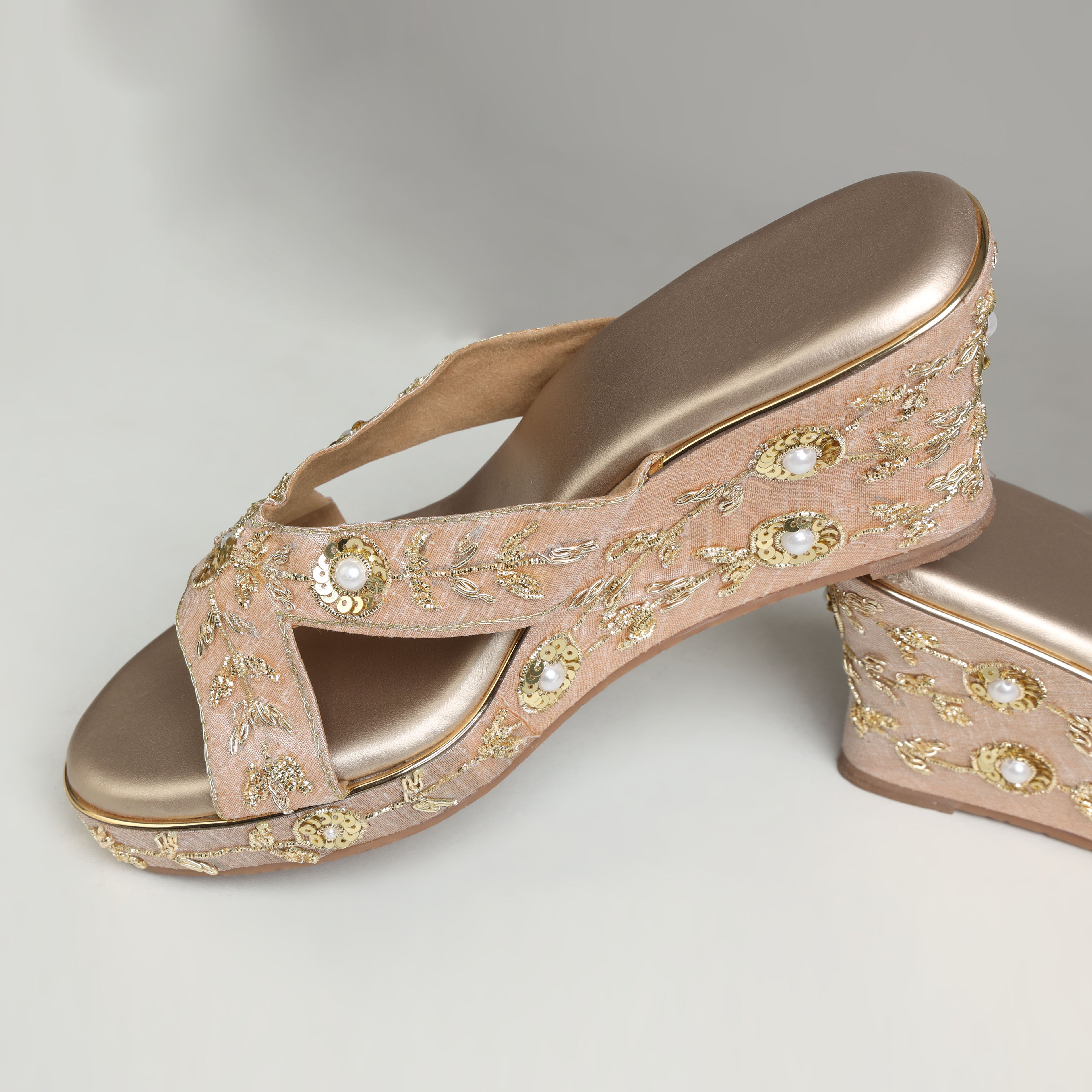 Pair of Riwaaz Noor rose gold zari embroidered pearl and sequin bridal wedge heels – flat lay product shot on cream satin surface with gold filigree box, gypsophila flowers and brass lantern in background