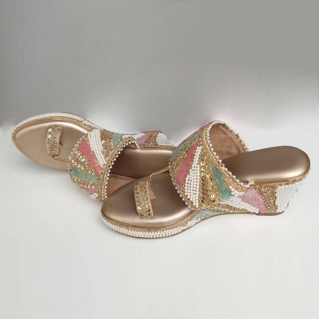 Pair of Riwaaz Meher dull rose gold bridal block heel sandals on white background – angled view showing champagne gold insole, toe-ring strap and full Nalli embroidered wedge body with pearl trim