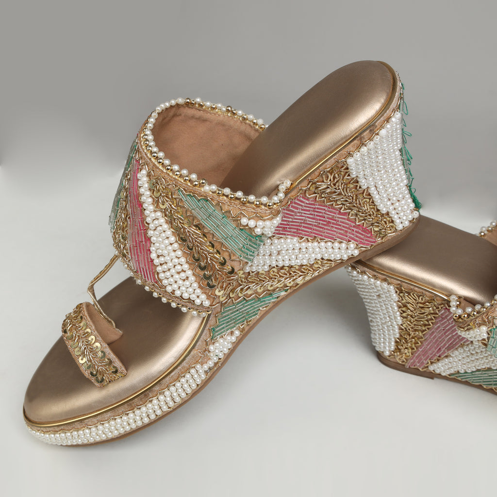 Pair of Riwaaz Meher dull rose gold Nalli embroidered pearl bridal block heel sandals – flat lay product shot on cream satin surface with gold filigree box, gypsophila flowers and brass lantern in background