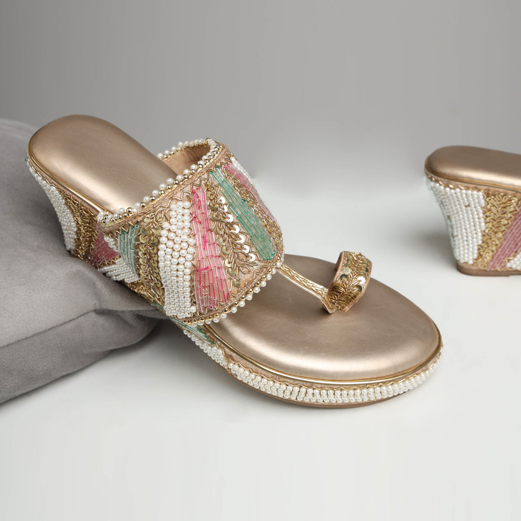 Model wearing Riwaaz Meher dull rose gold Nalli embroidered pearl bridal block heel sandals with peach sequin salwar – close-up foot shot showing multicolour beaded strap and pearl-trimmed wedge on marble floor
