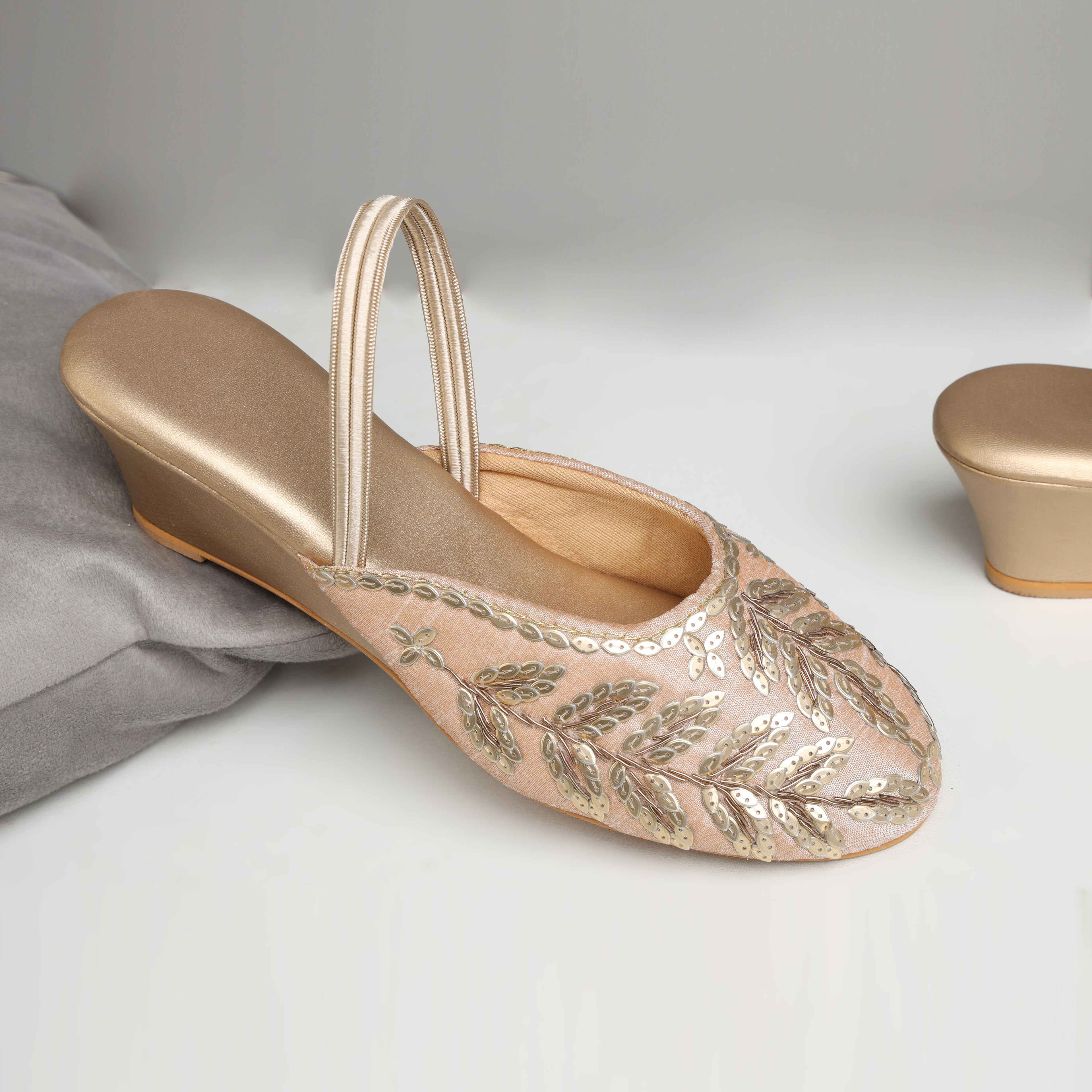 Model wearing Riwaaz Zehra dull gold sequin leaf embroidered slingback wedge mules with ivory embroidered kurta set – close-up foot shot on jute rug showing full sequin leaf embroidery and gold wedge