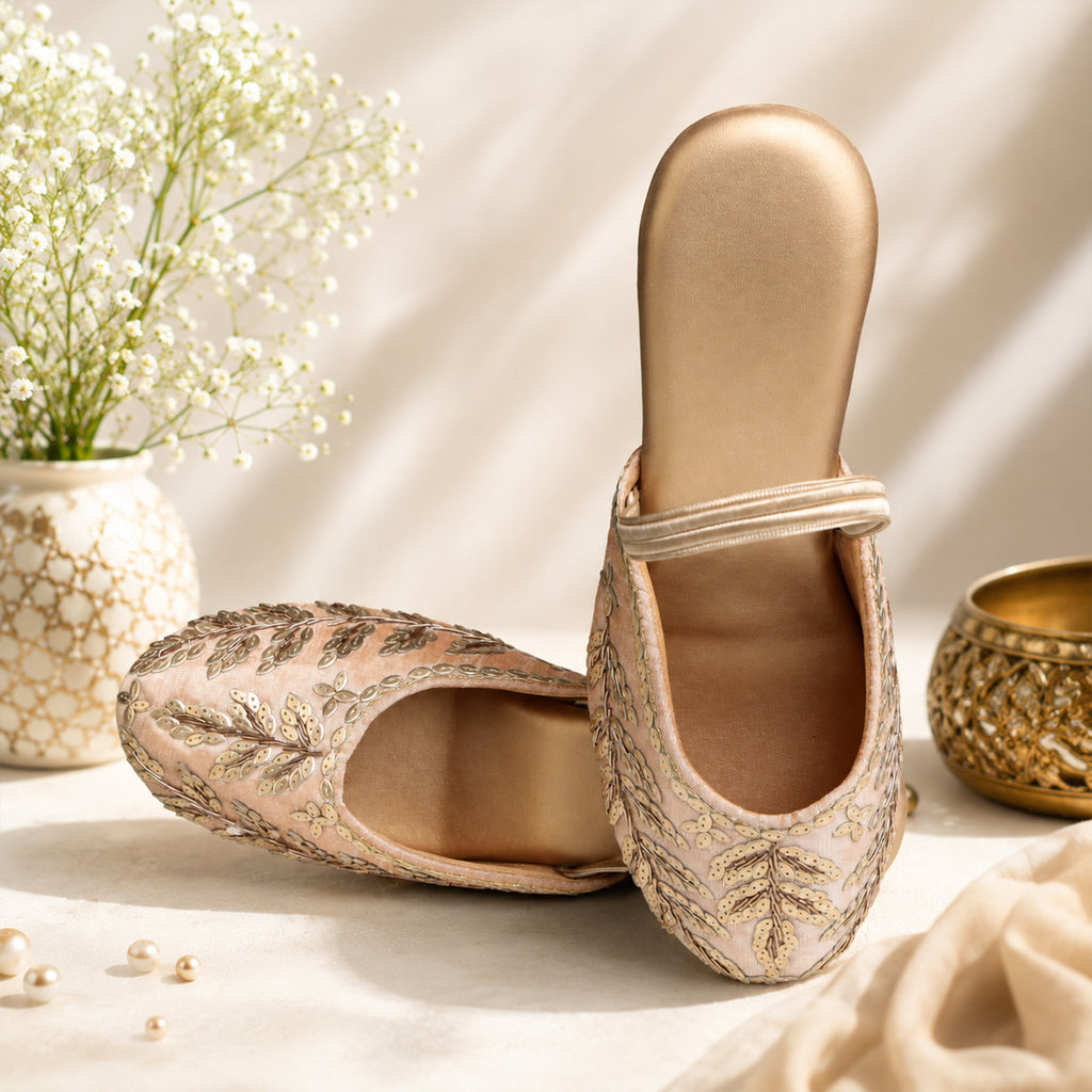 Model seated in ivory embroidered kurta with dupatta wearing Riwaaz Zehra dull gold sequin leaf embroidered slingback wedge mules – full lifestyle shot in warm Indian interior with brass lantern and rattan chair