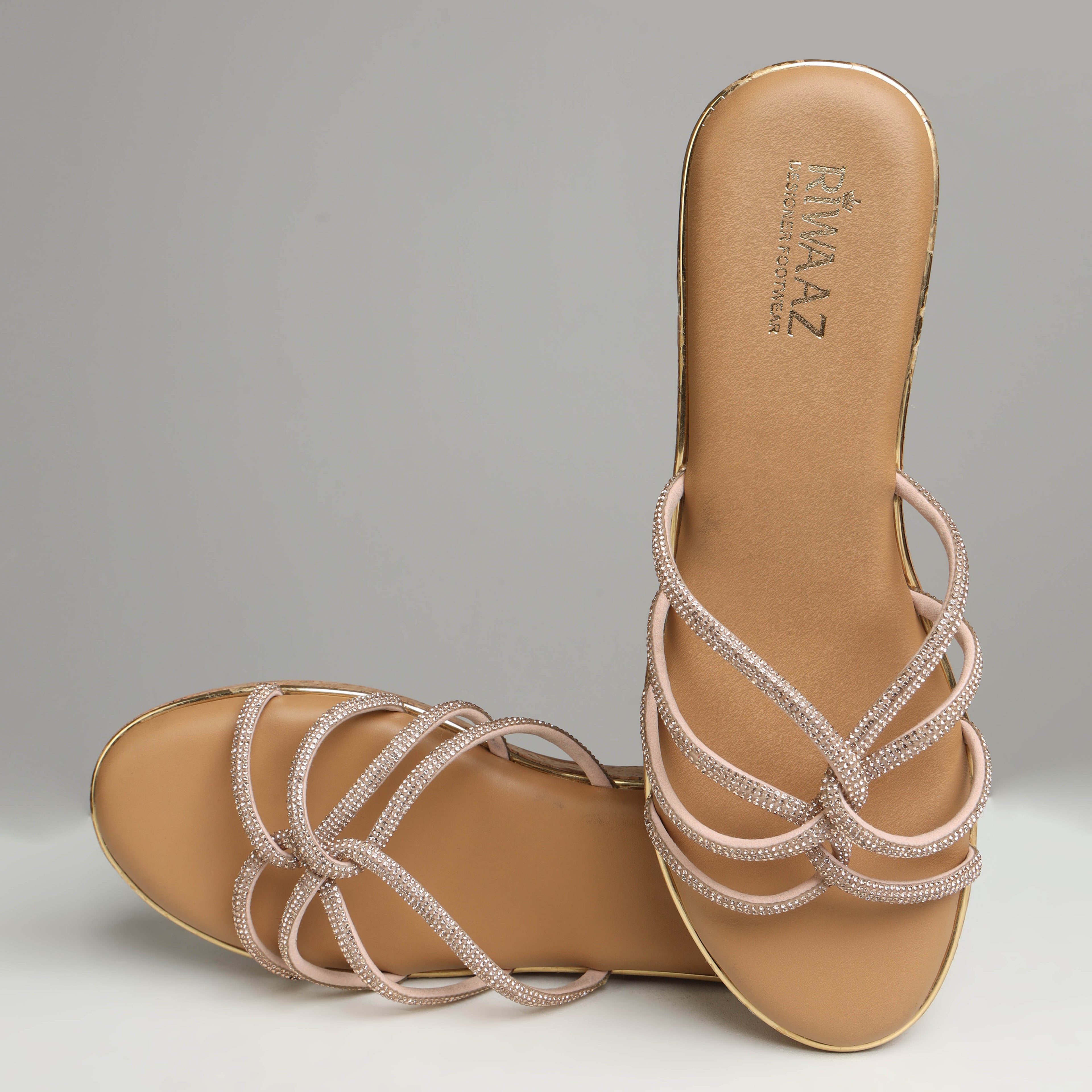 Pair of Riwaaz Zarina Glow dark beige crystal crossover cork wedge platforms on grey background – front angled view showing open-toe design, full rhinestone crossover strap and natural cork wedge with gold trim