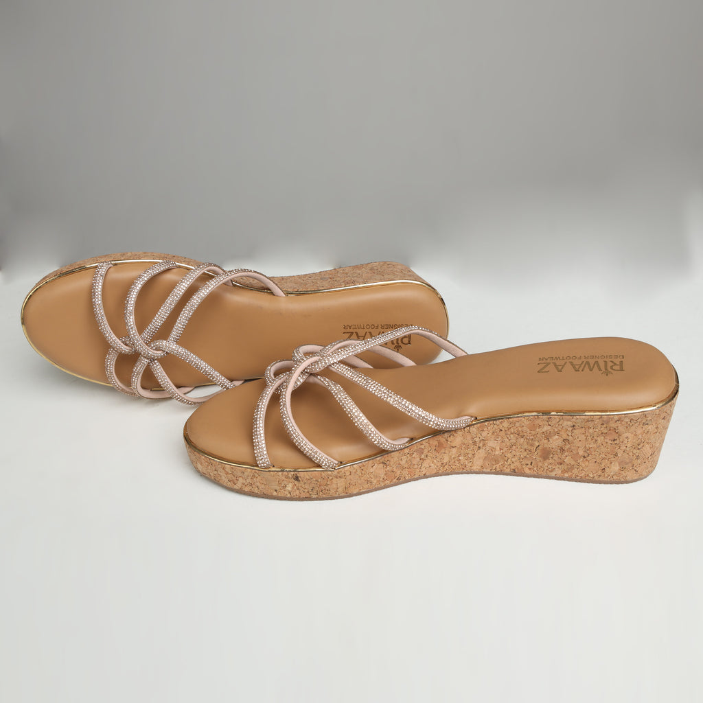 Pair of Riwaaz Zarina Glow dark beige crystal crossover cork wedge platforms on grey background – top-down view showing tan cushioned insole with Riwaaz branding and full rhinestone crossover strap detail