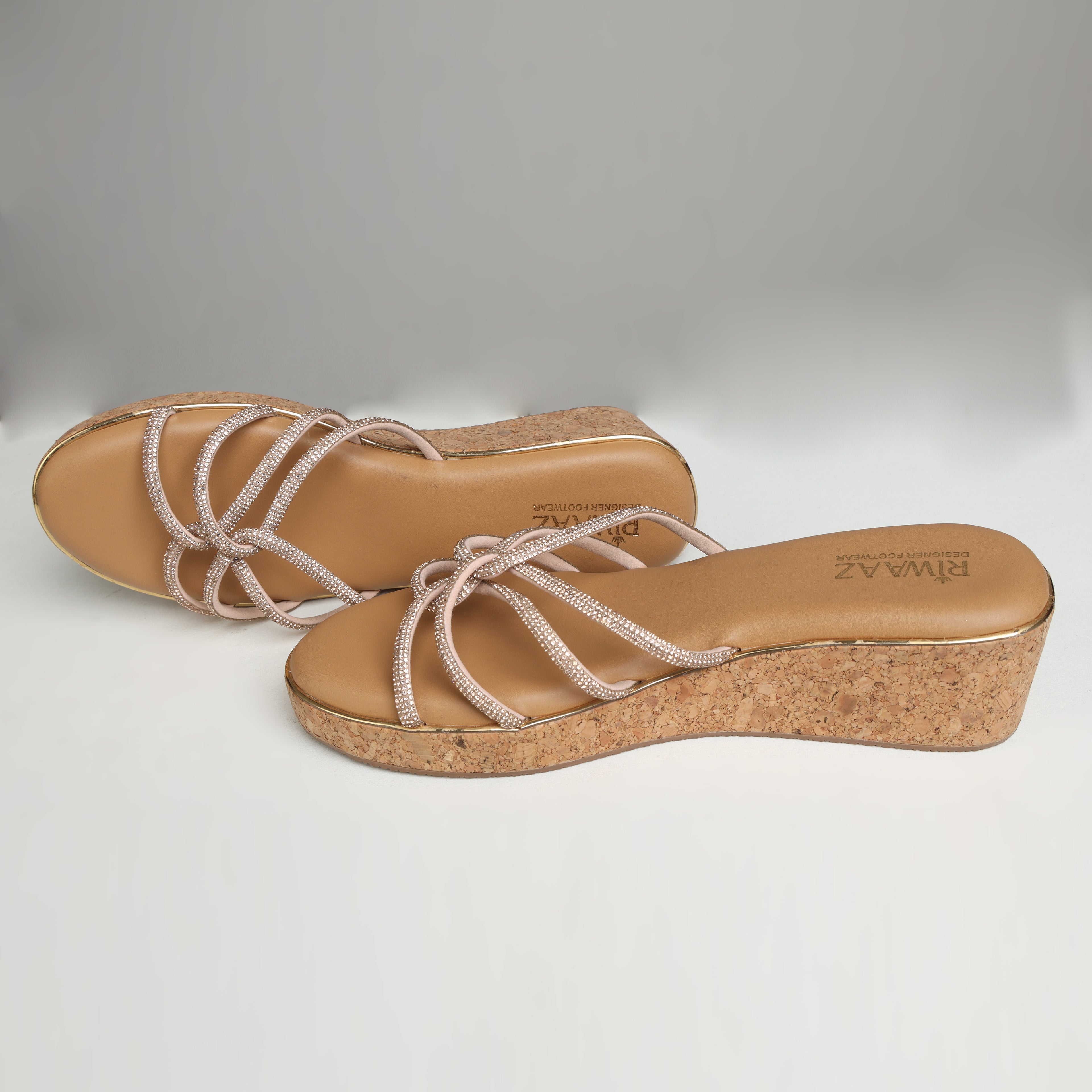 Pair of Riwaaz Zarina Glow dark beige crystal crossover cork wedge platforms on grey background – top-down view showing tan cushioned insole with Riwaaz branding and full rhinestone crossover strap detail