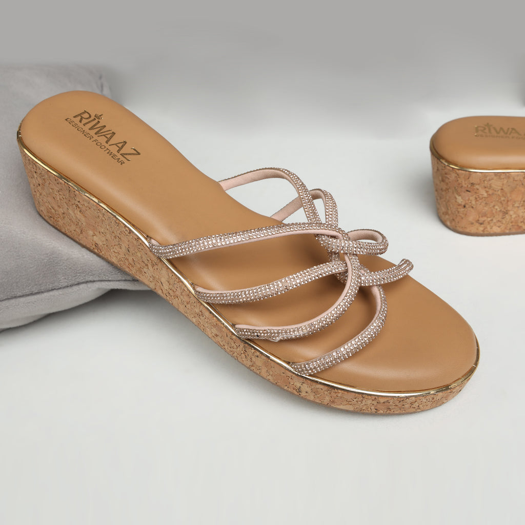 Model wearing Riwaaz Zarina Glow dark beige crystal crossover cork wedge platforms with ivory embroidered kurta set – full lifestyle shot seated on stone steps in ornate Indian haveli with brass diyas and marigold petals