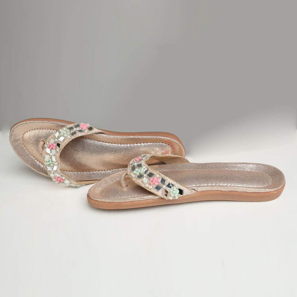 Riwaaz Misha dull rose gold mirror work flip flops styled with white gypsophila flowers, pearl necklace and brass trinket box on marble surface
