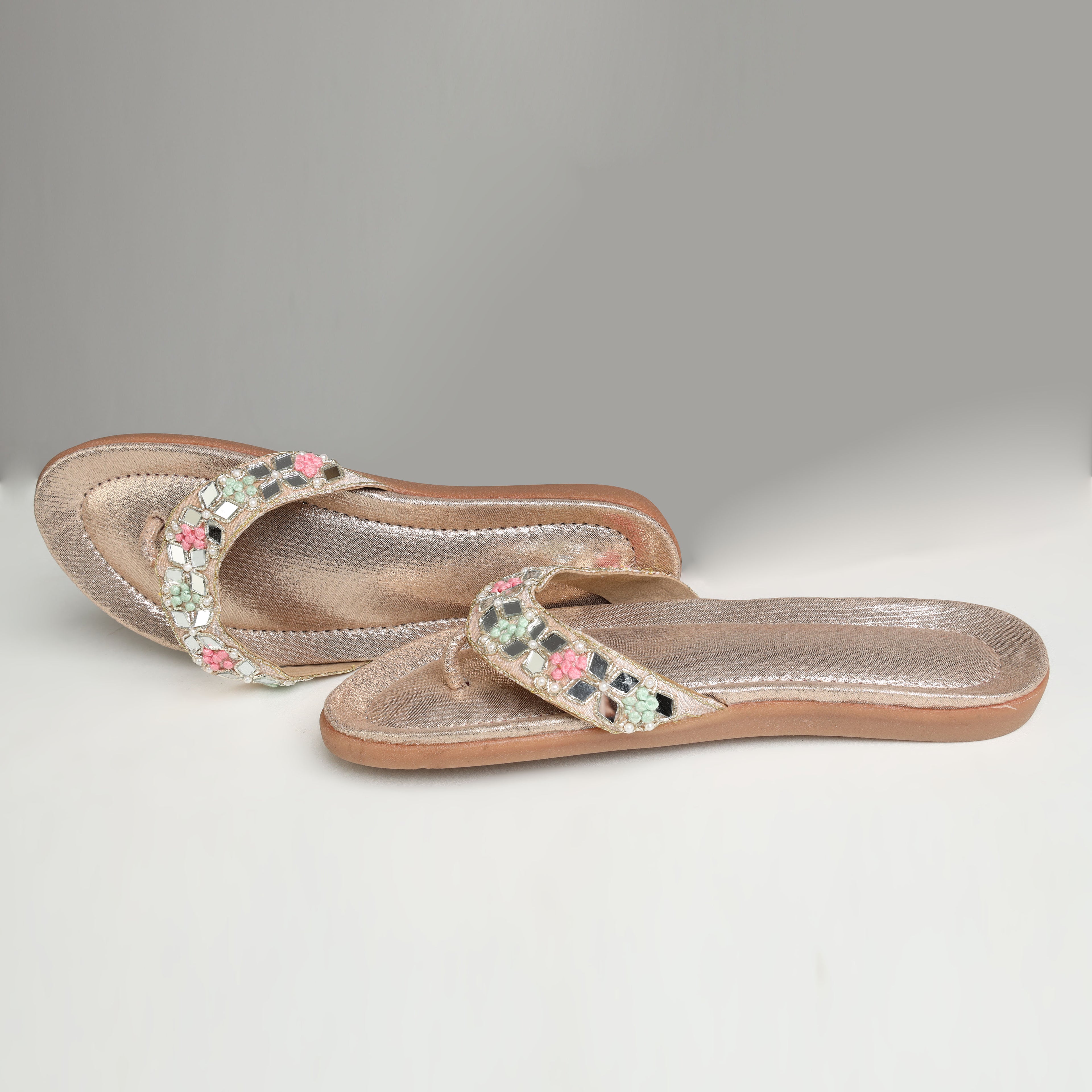 Riwaaz Misha dull rose gold mirror work flip flops styled with white gypsophila flowers, pearl necklace and brass trinket box on marble surface