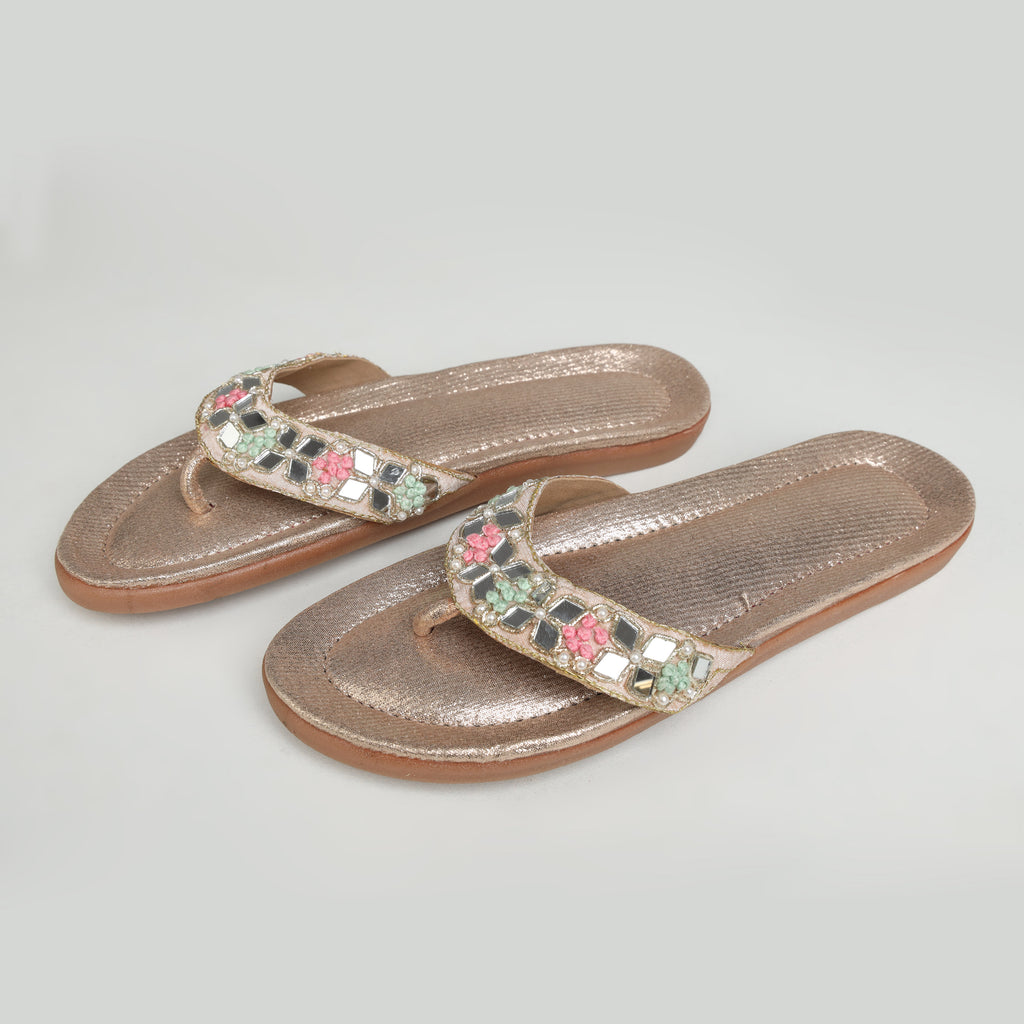 Model seated in peach embroidered salwar suit wearing Riwaaz Misha dull rose gold mirror work flip flops – full lifestyle shot in traditional Indian courtyard setting