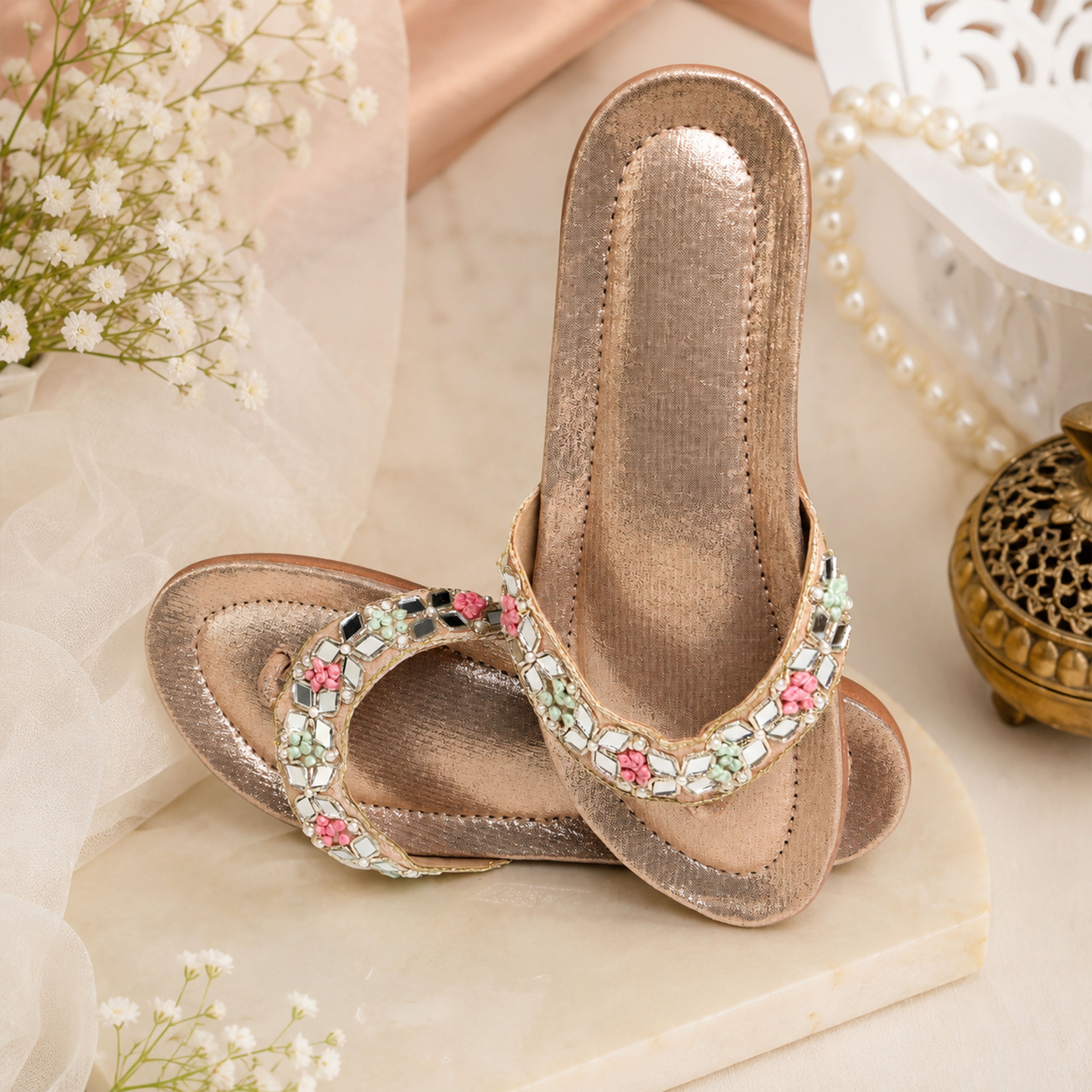 Pair of Riwaaz Misha dull rose gold mirror work flip flops – angled view showing mirror work and pastel French knot detail on strap with shimmer footbed