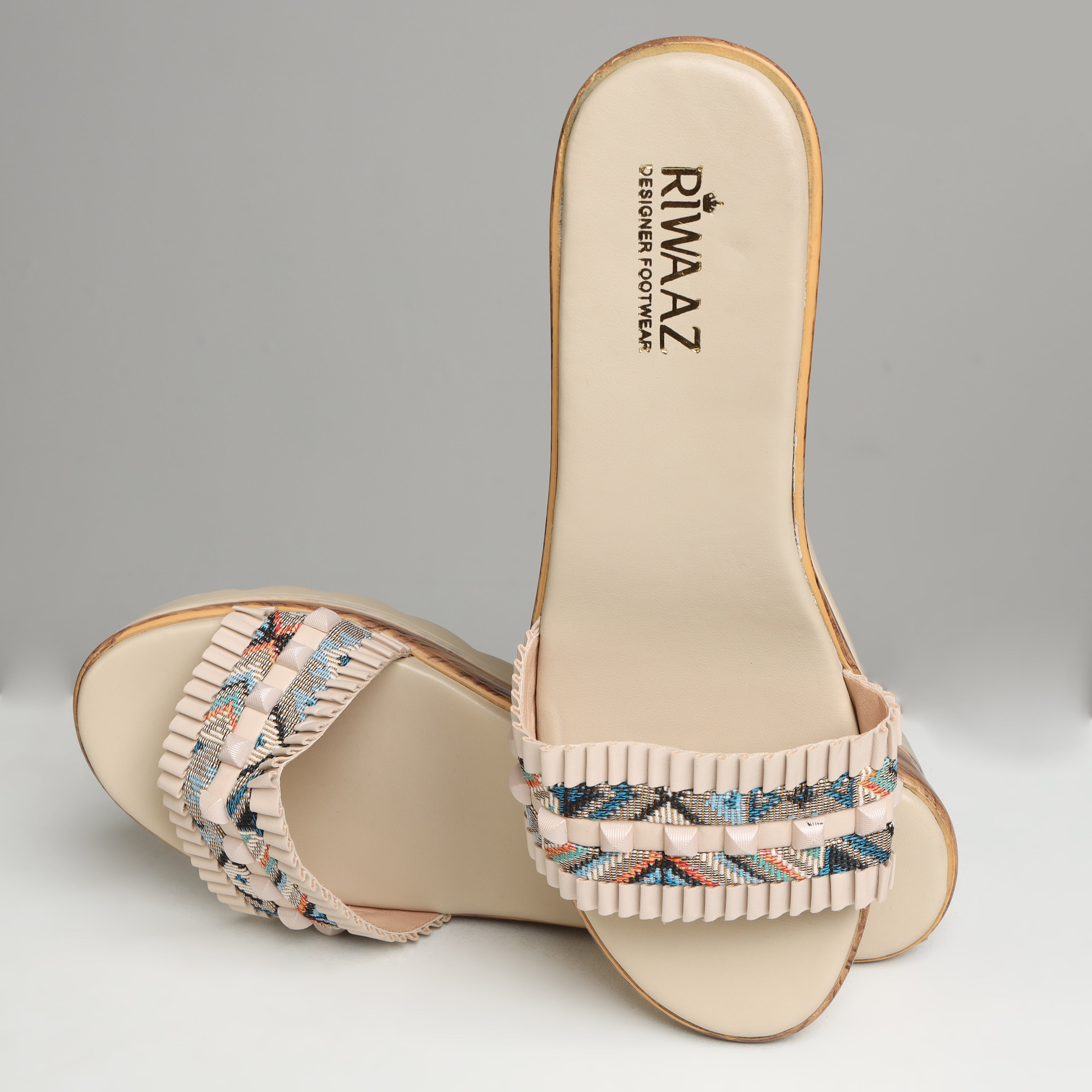 Pair of Riwaaz Elara cream printed pleated strap wedge slides on grey background – front angled view showing open-toe design, full multicolour geometric print strap with cream pleated trim and wedge sole