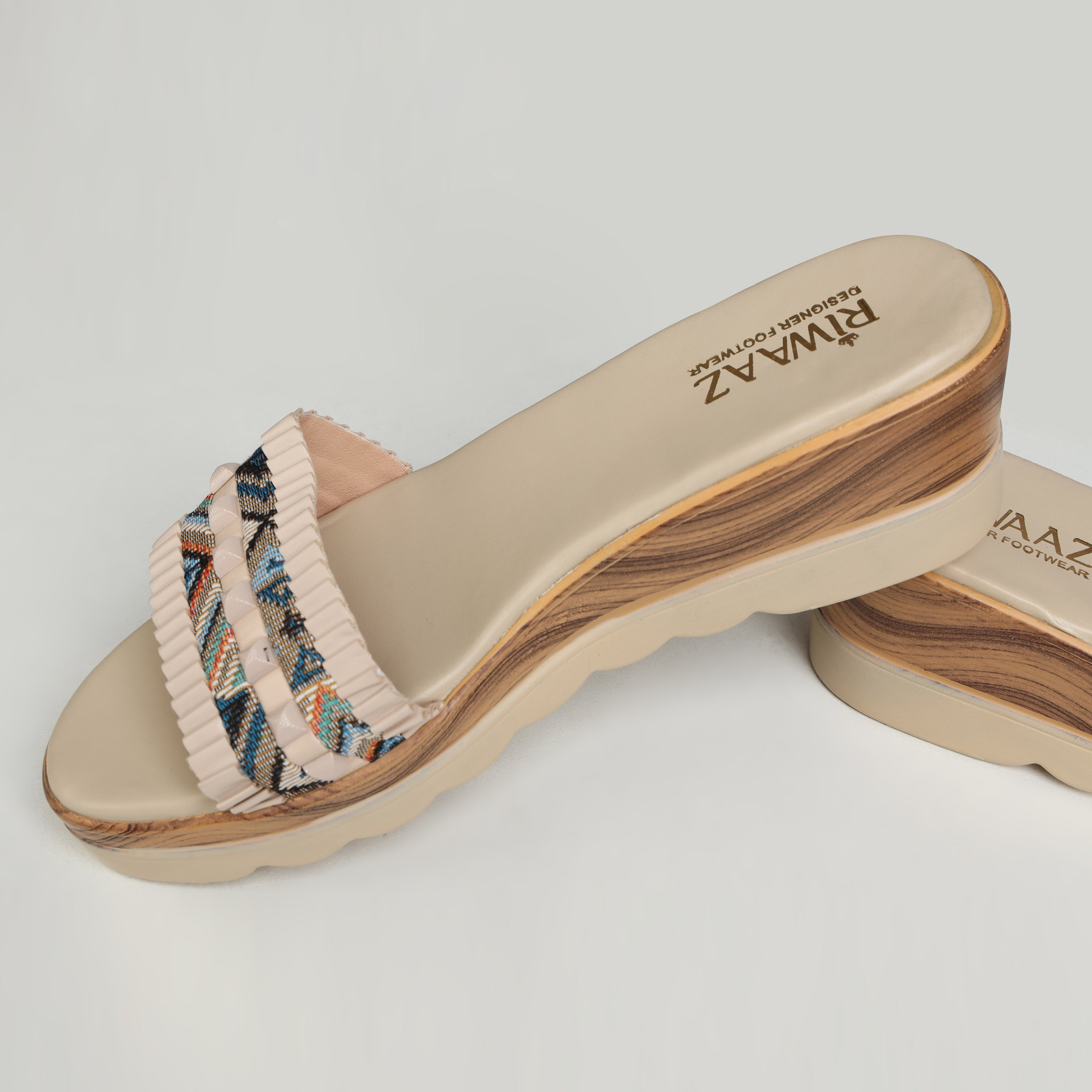 Pair of Riwaaz Elara cream printed pleated strap wedge slides – lifestyle flat lay on sandy linen surface with gypsophila flowers, rattan tray and Bloom book showing top-down view of geometric print pleated strap