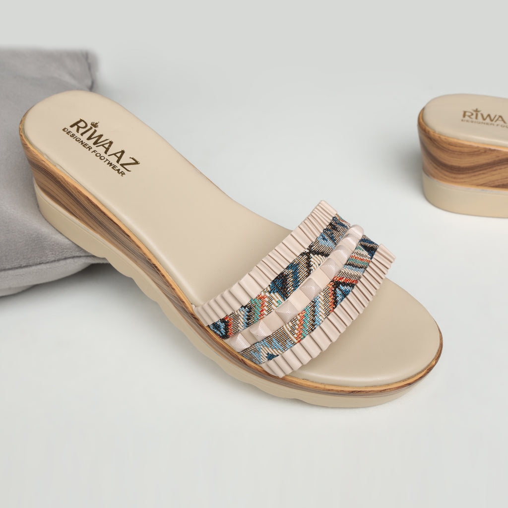 Model wearing Riwaaz Elara cream printed pleated strap wedge slides with ivory embroidered kurta set – close-up foot shot on stone floor showing multicolour geometric print strap with cream pleated trim and wedge sole