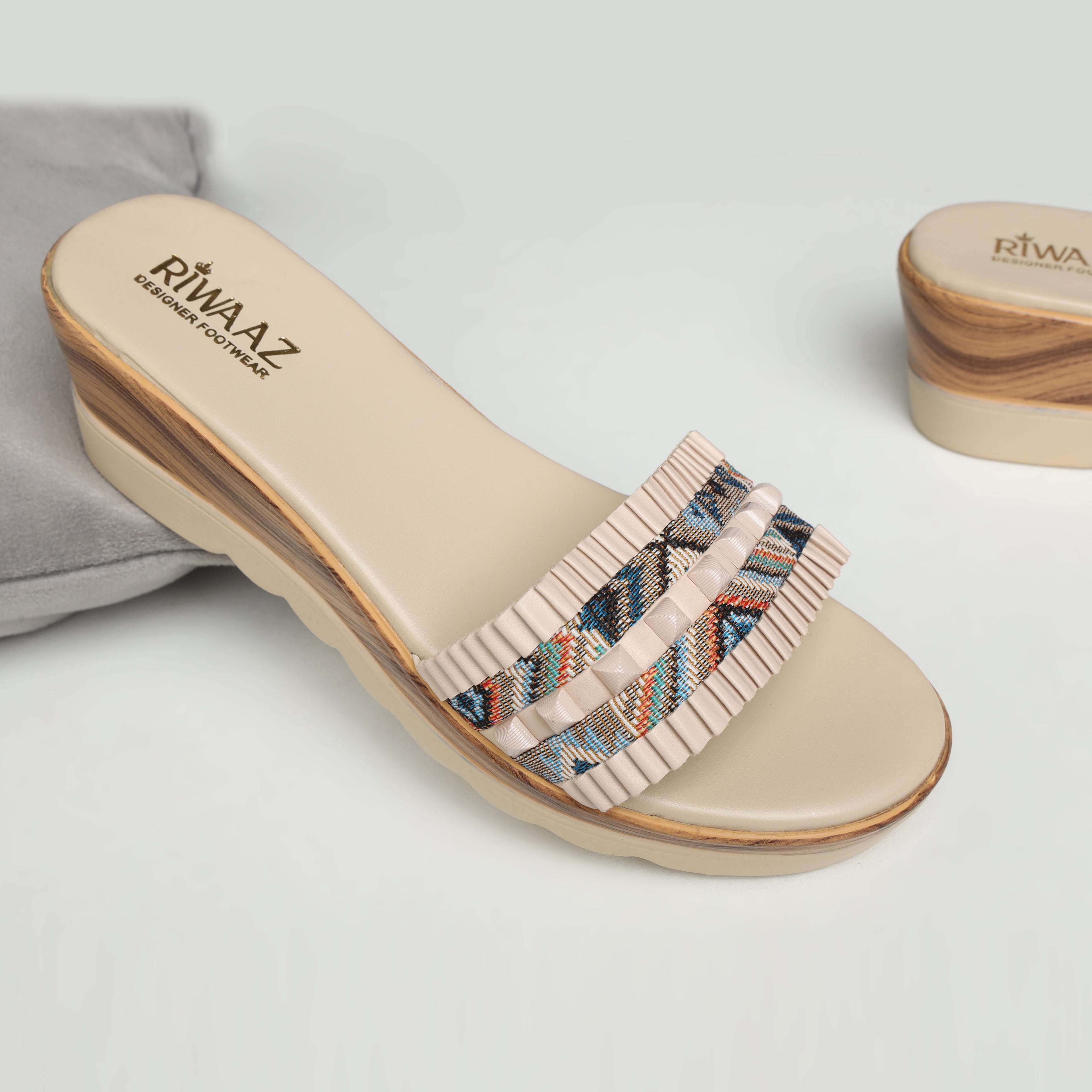 Model wearing Riwaaz Elara cream printed pleated strap wedge slides with ivory embroidered kurta set – close-up foot shot on stone floor showing multicolour geometric print strap with cream pleated trim and wedge sole